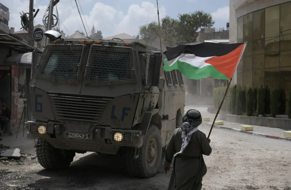 A man waves Palestenian flag as an israeli armored vehicle moves in a street during military raid in the west bank refugee camp of Nur Shams, Tulkarem (Photo/AP news)